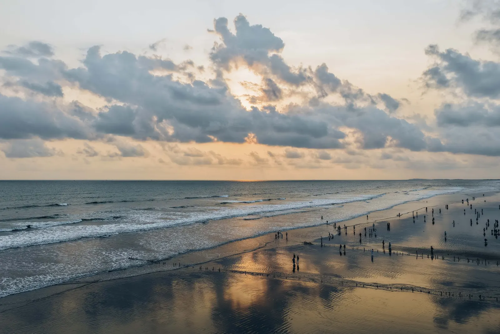 Walkers on the wet sand at Cox's Bazar as the sun sets behind the clouds