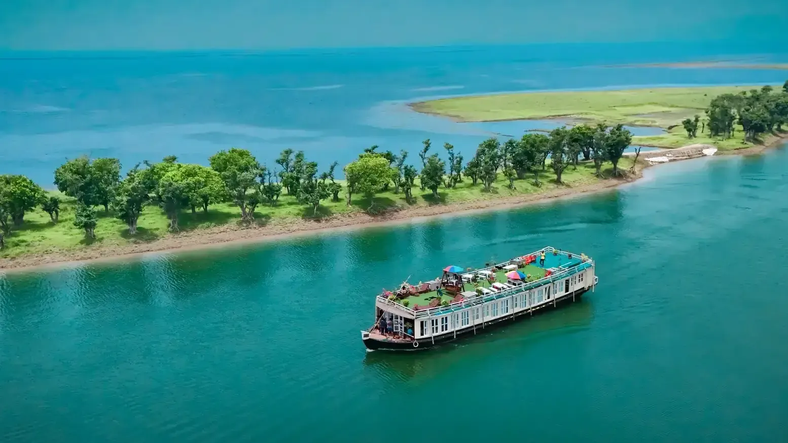 A houseboat on turquoise water beside a line of trees at Tanguar Haor